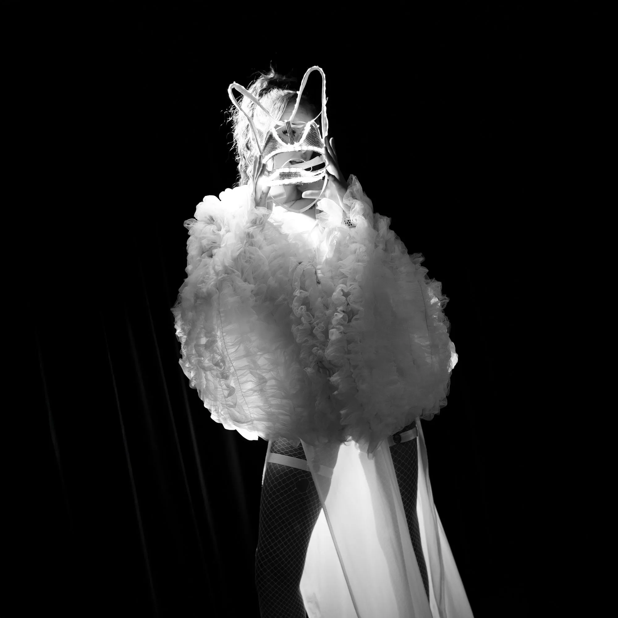 Tanečnice ve výrazném scénickém kostýmu inspirovaném světelnými show 80. a 90. let vytváří kontrastní siluetu v temném prostoru klubu.