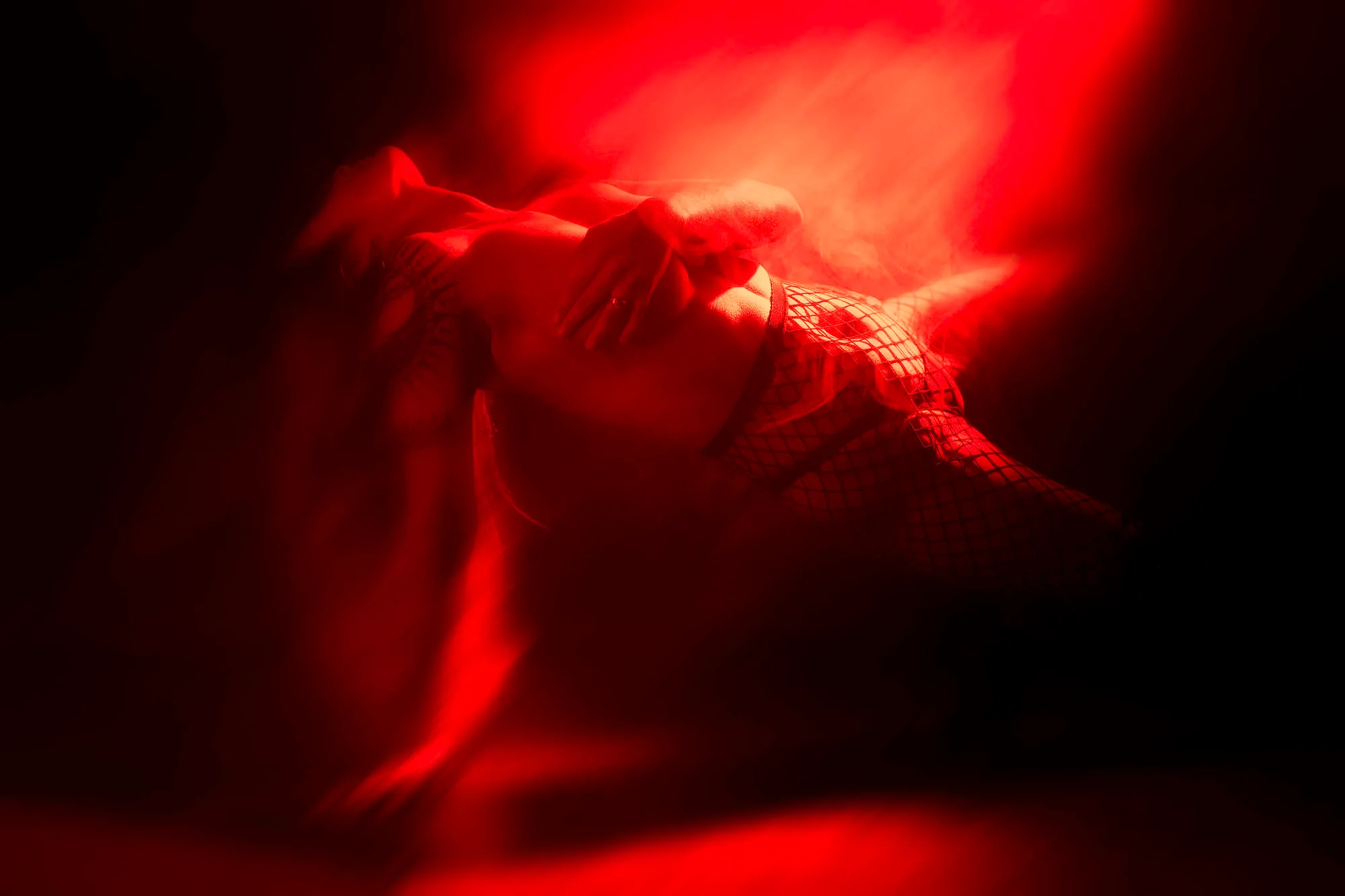 A dancer performing a movement pose during training for a bachelor party performance inside the club. The scene is illuminated with intense red lighting, and visible stage smoke surrounds the figure.